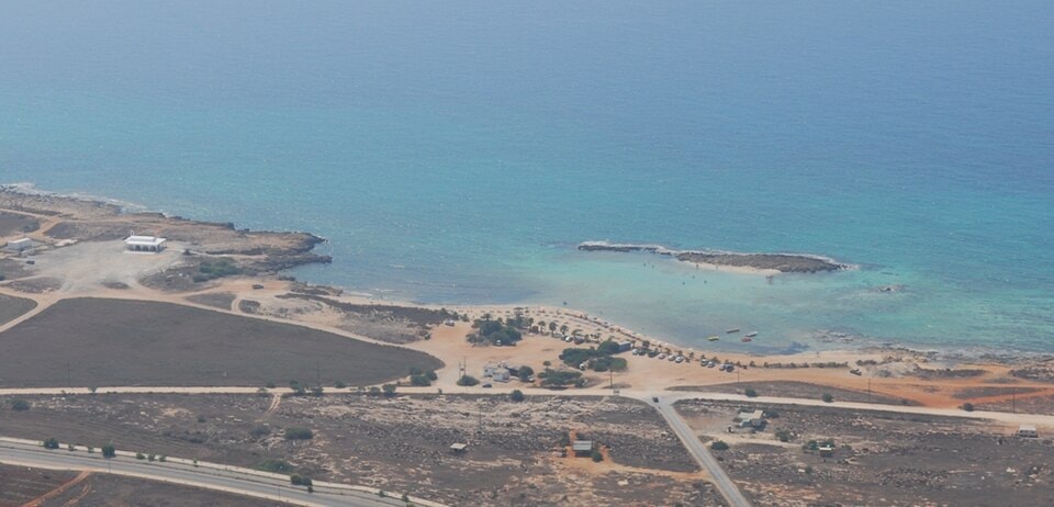 An aerial shot of Ayia Thekla beach, showing its narrow crescent of sand, surrounding dry landscape, and nearby roads.