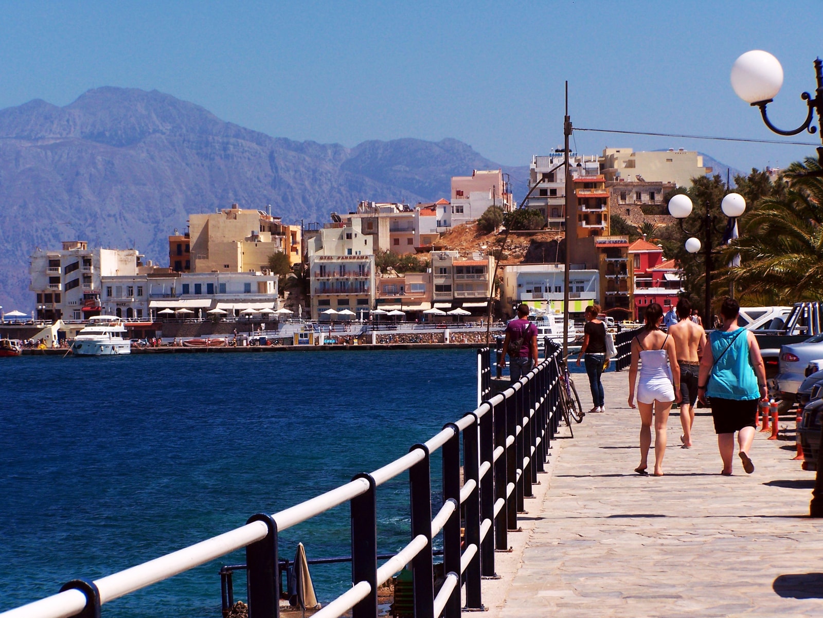 A promenade in Agios Nikolaos showing the walkway, harbor, and rugged mountains in the background.