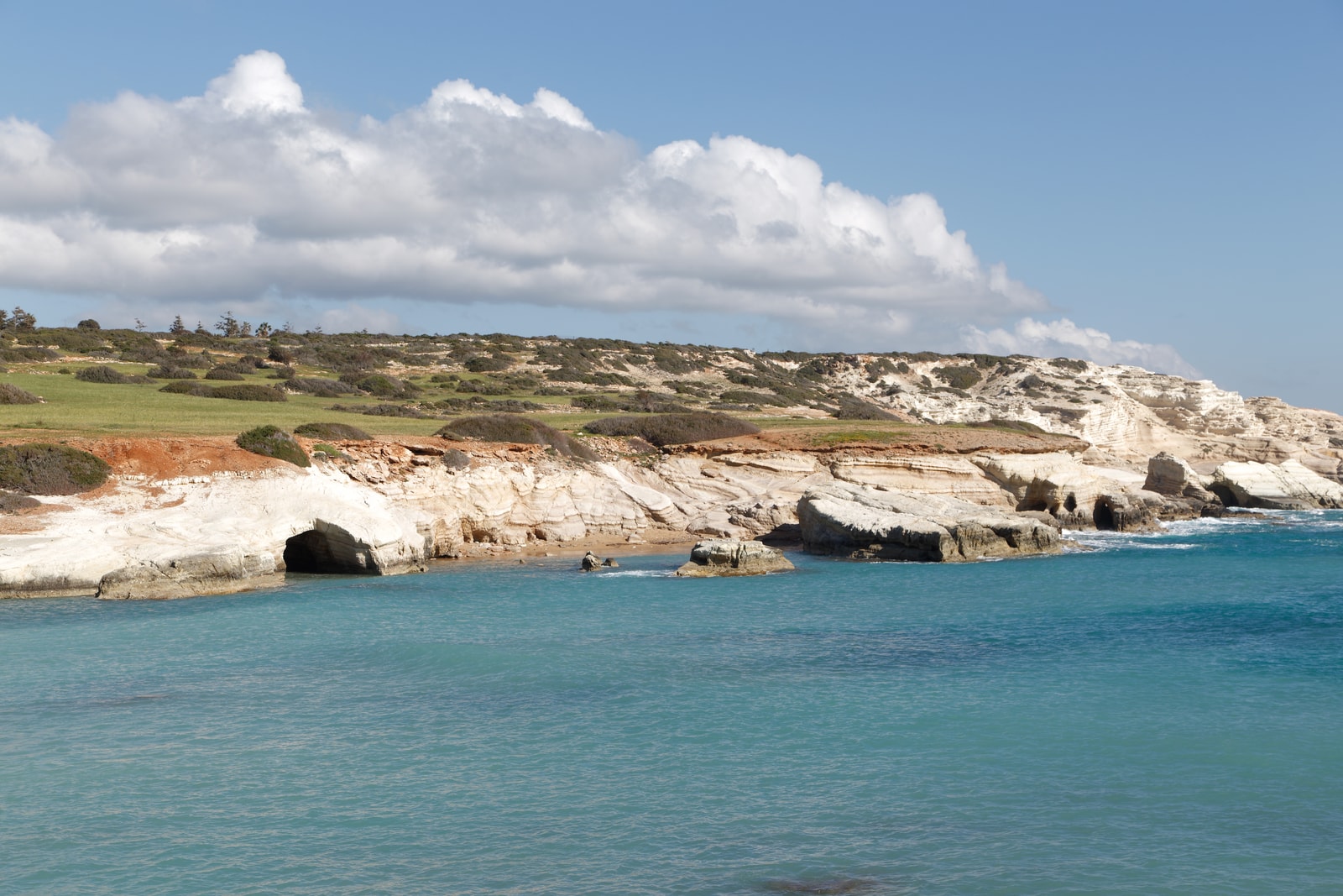 A wide view of a dramatic coastline with pale cliffs and dark sea cave openings under a sky filled with clouds.
