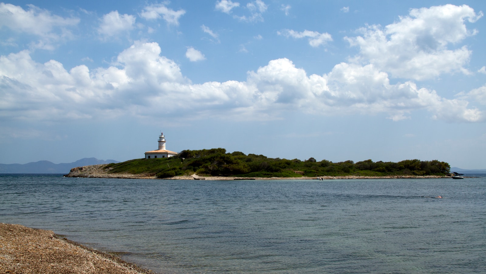 A small, tree-covered island with a lighthouse sits in the bay under a dramatic, cloudy sky.