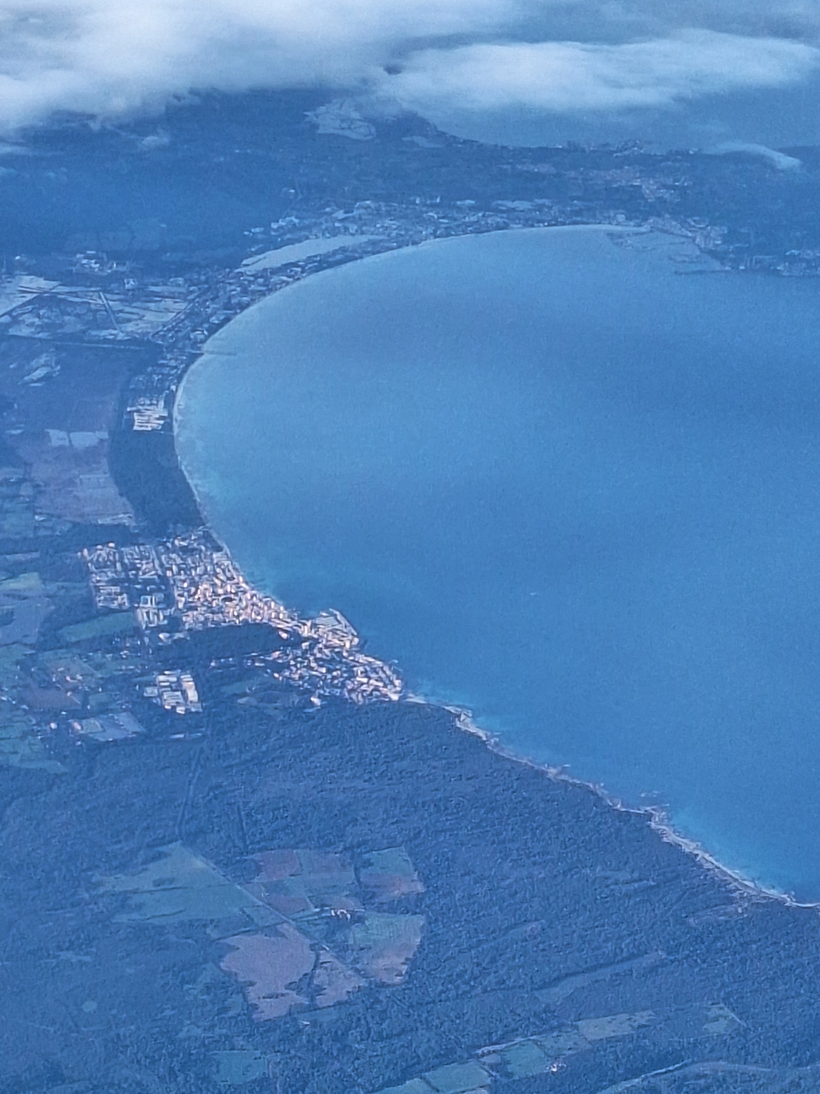 An aerial view shows a long crescent of sandy beach along a turquoise bay, with resorts and green wetlands visible inland.