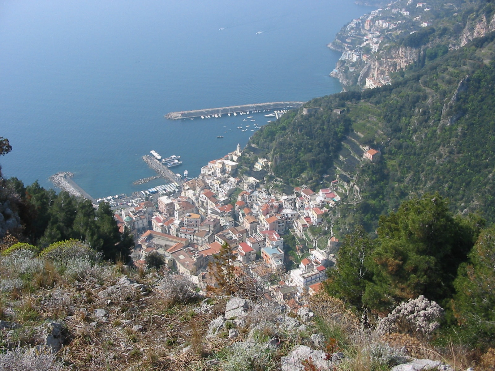An elevated view of Amalfi's harbor, beach, and compact town nestled between cliffs.