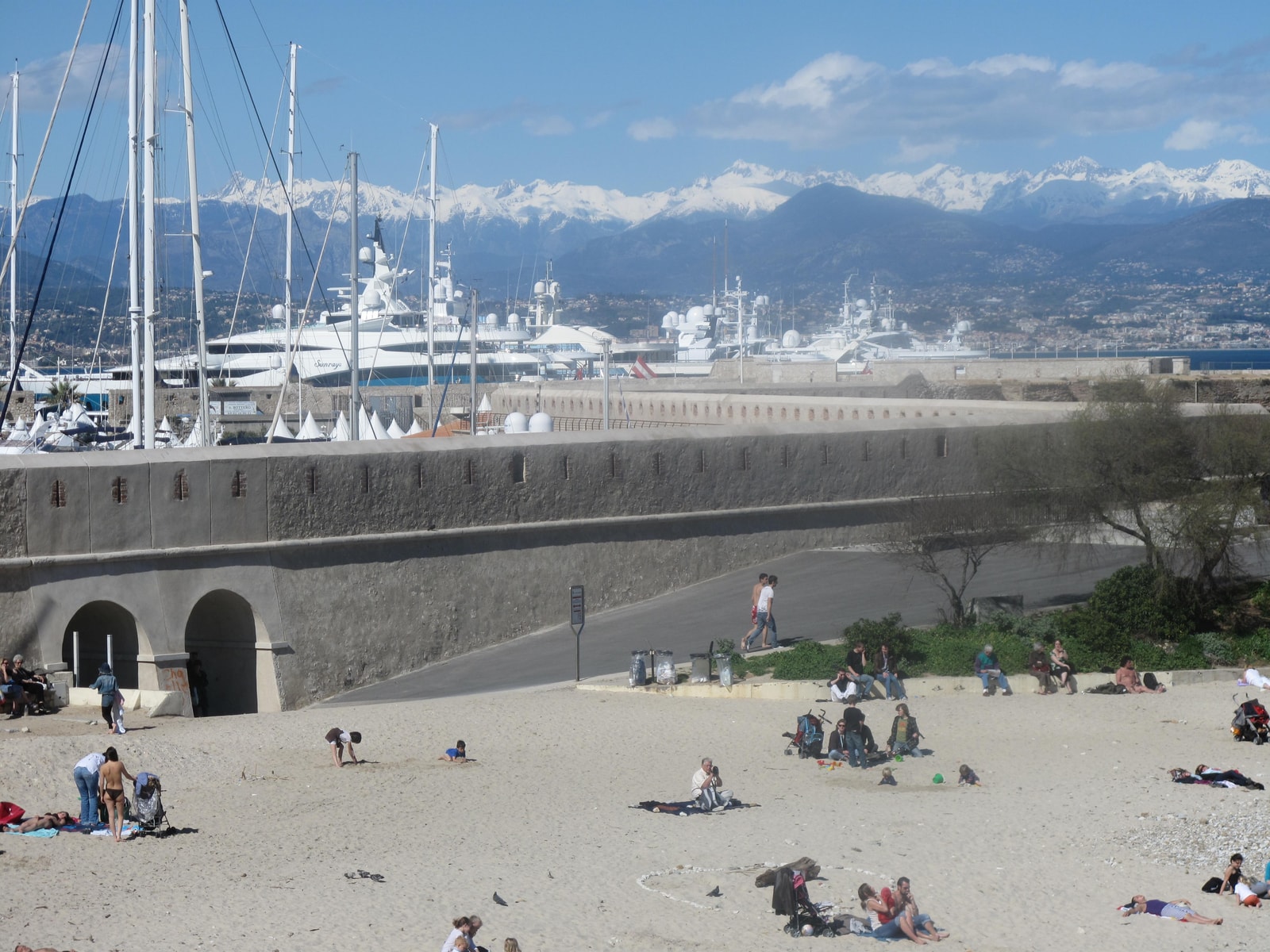 The stone ramparts of Antibes border a port filled with yachts, with snow-capped mountains visible in the distance.