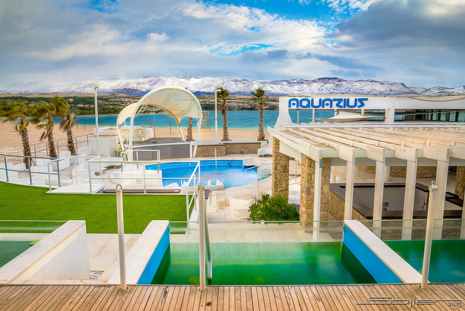 The modern, open-air Aquarius Club with its pool and palm trees, set against the backdrop of snow-capped mountains.