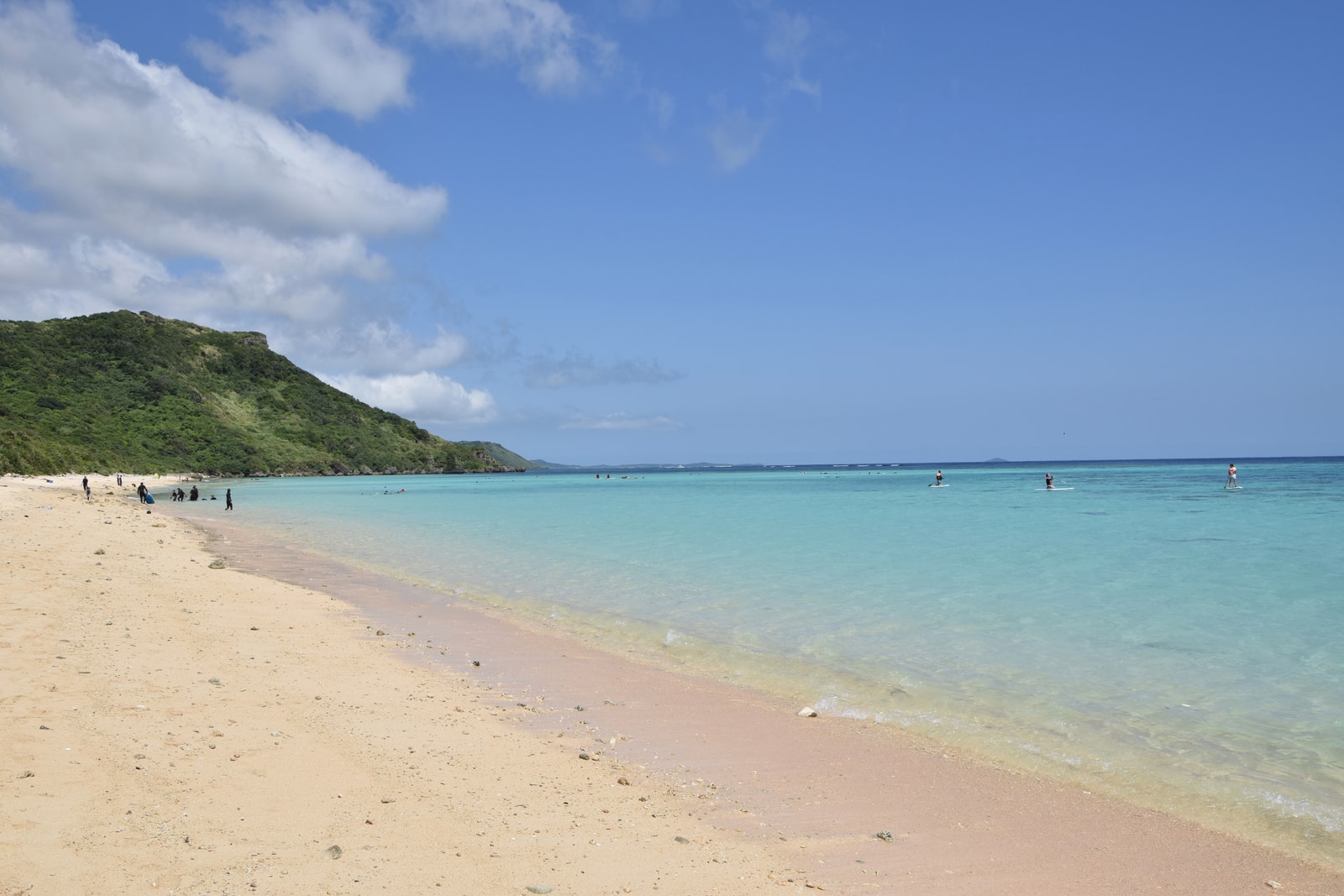 A sunny beach with clear, shallow water and unique rock formations in the sea.