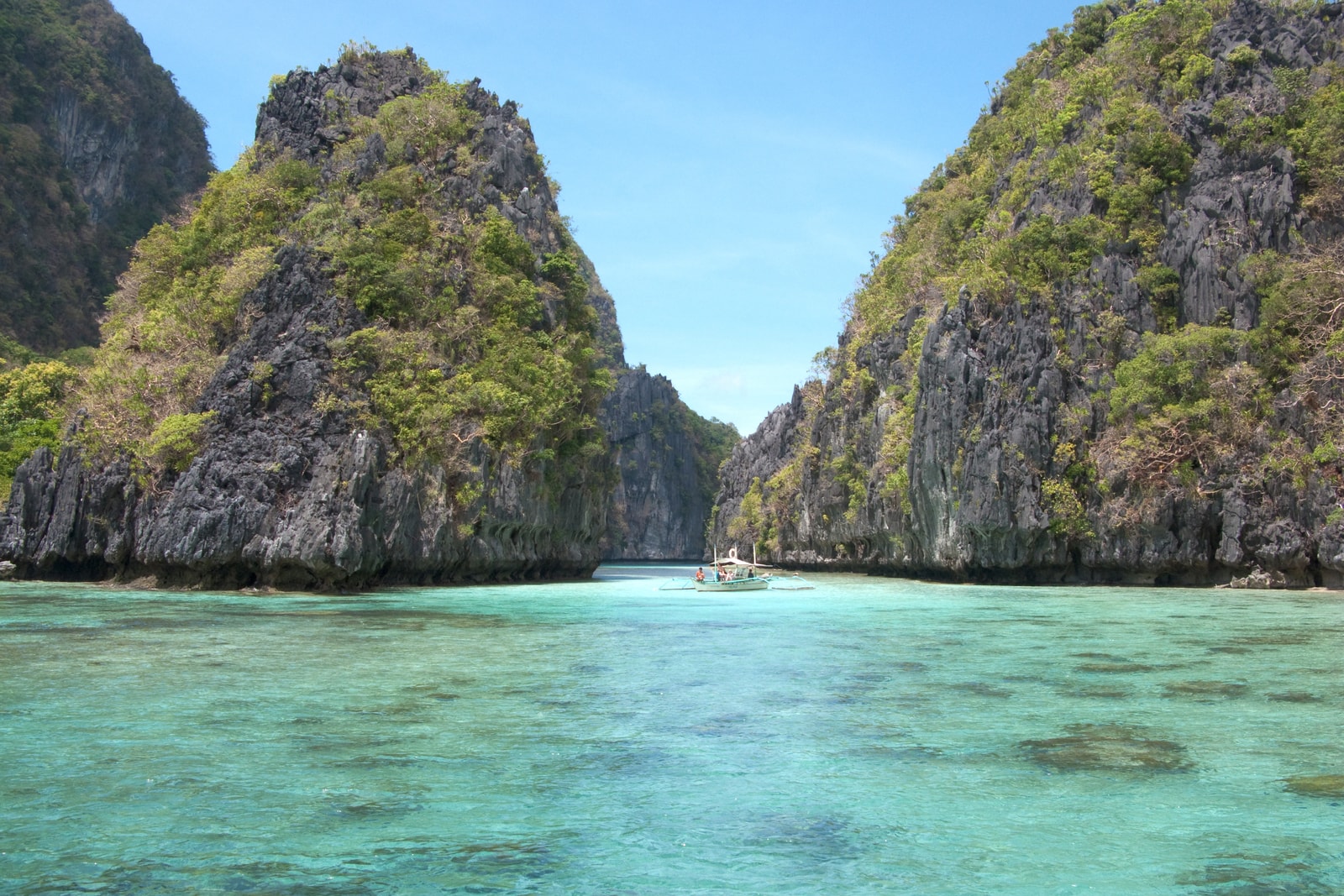 Several outrigger boats navigate a channel between high limestone cliffs in Bacuit Bay.