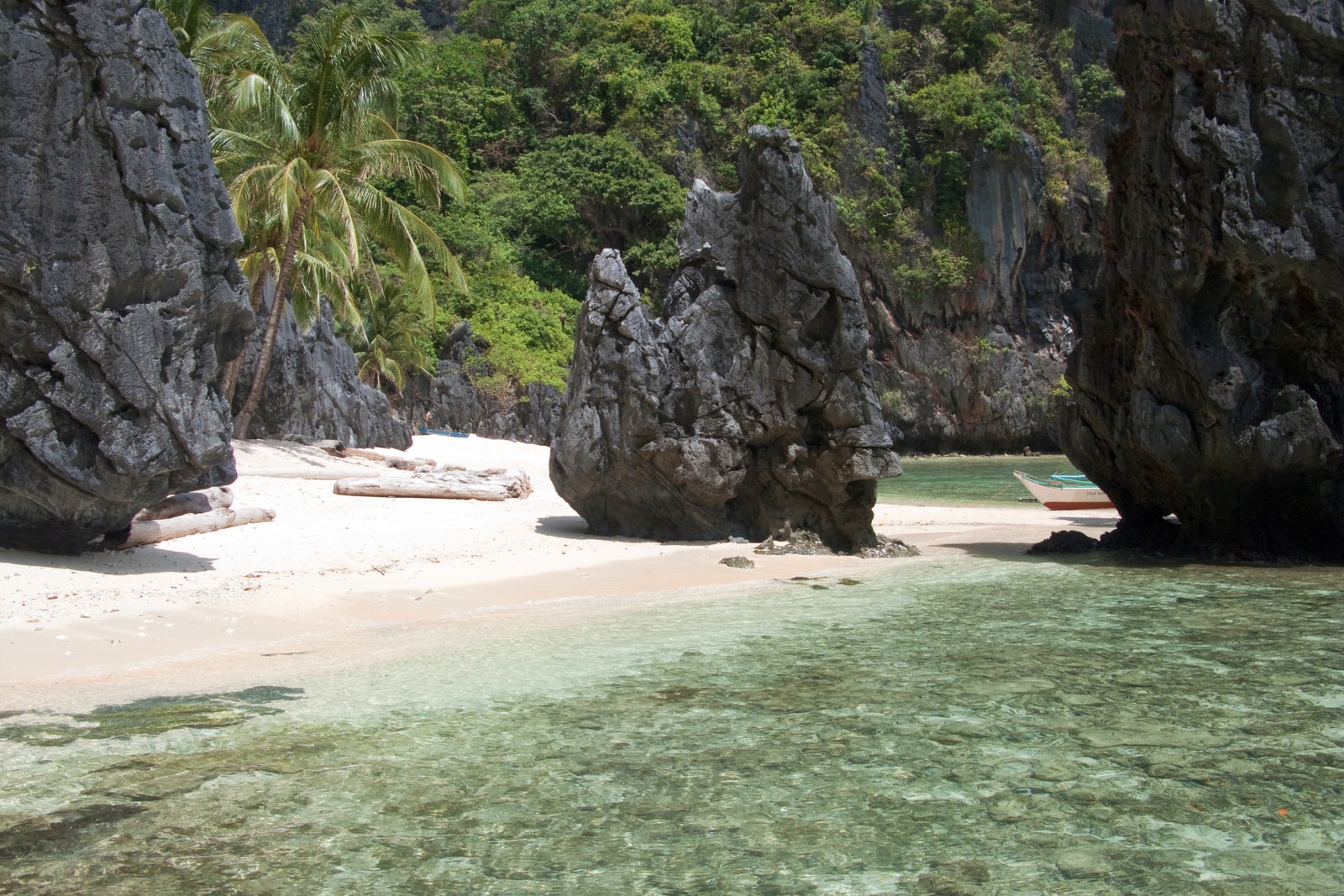 A small, secluded beach with light sand is sheltered by tall, jungle-covered limestone rock formations.