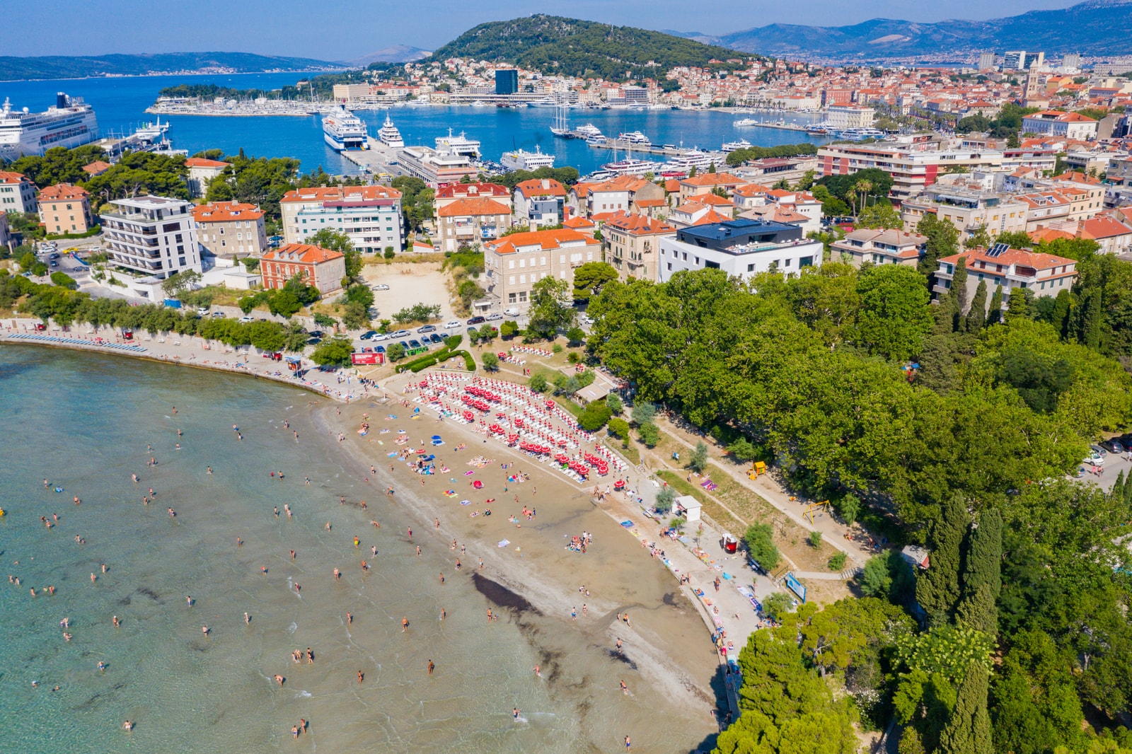 Panoramic aerial view of Bačvice Bay, Split, Croatia showing the resort bay, coastal woodlands, and busy ferry harbor.