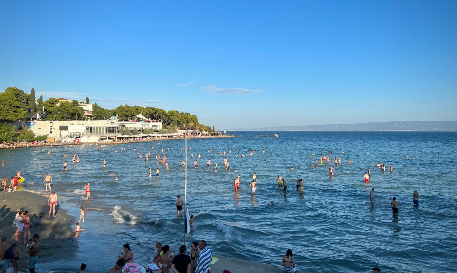 Elevated view of numerous beachgoers wading through the shallow sandy bay at Bačvice Beach.