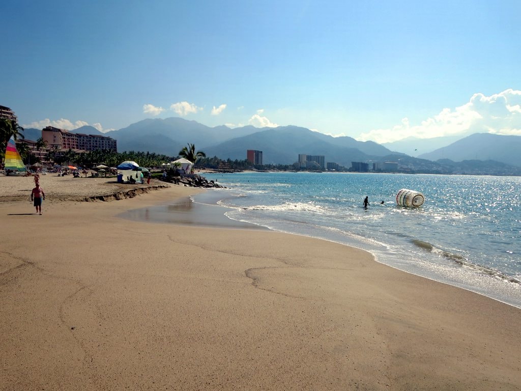 A wide beach curves around Banderas Bay with lush green mountains in the background.