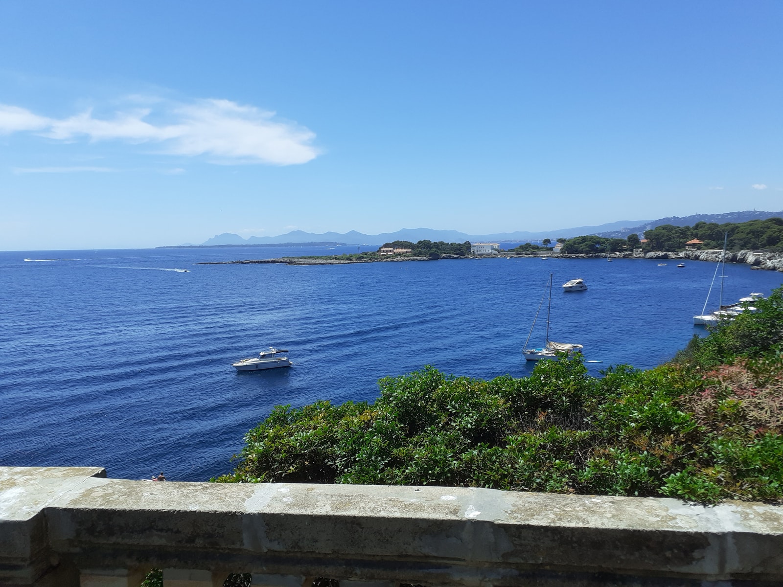 A scenic view of a bay with clear turquoise water, framed by stone balustrades and lush green foliage.