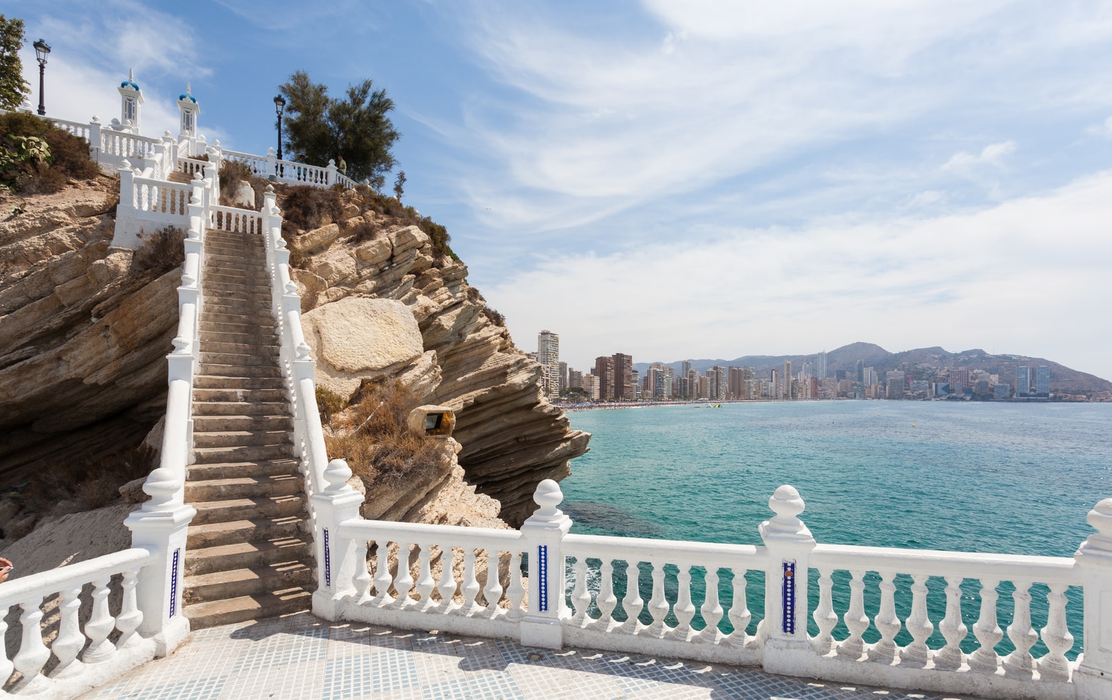 A dramatic white staircase cascades down a rugged cliffside toward the blue Mediterranean Sea.