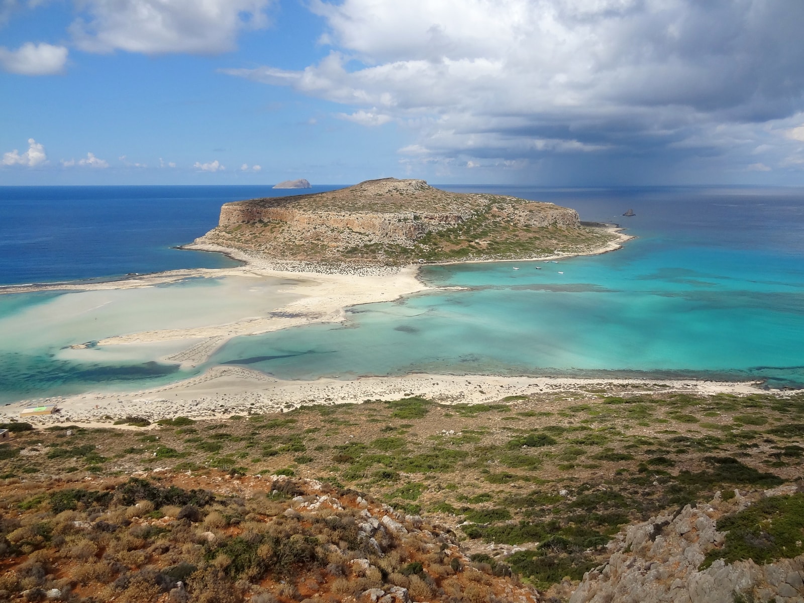 The shallow, clear turquoise waters of Balos Lagoon meet the pinkish-white sand shore.