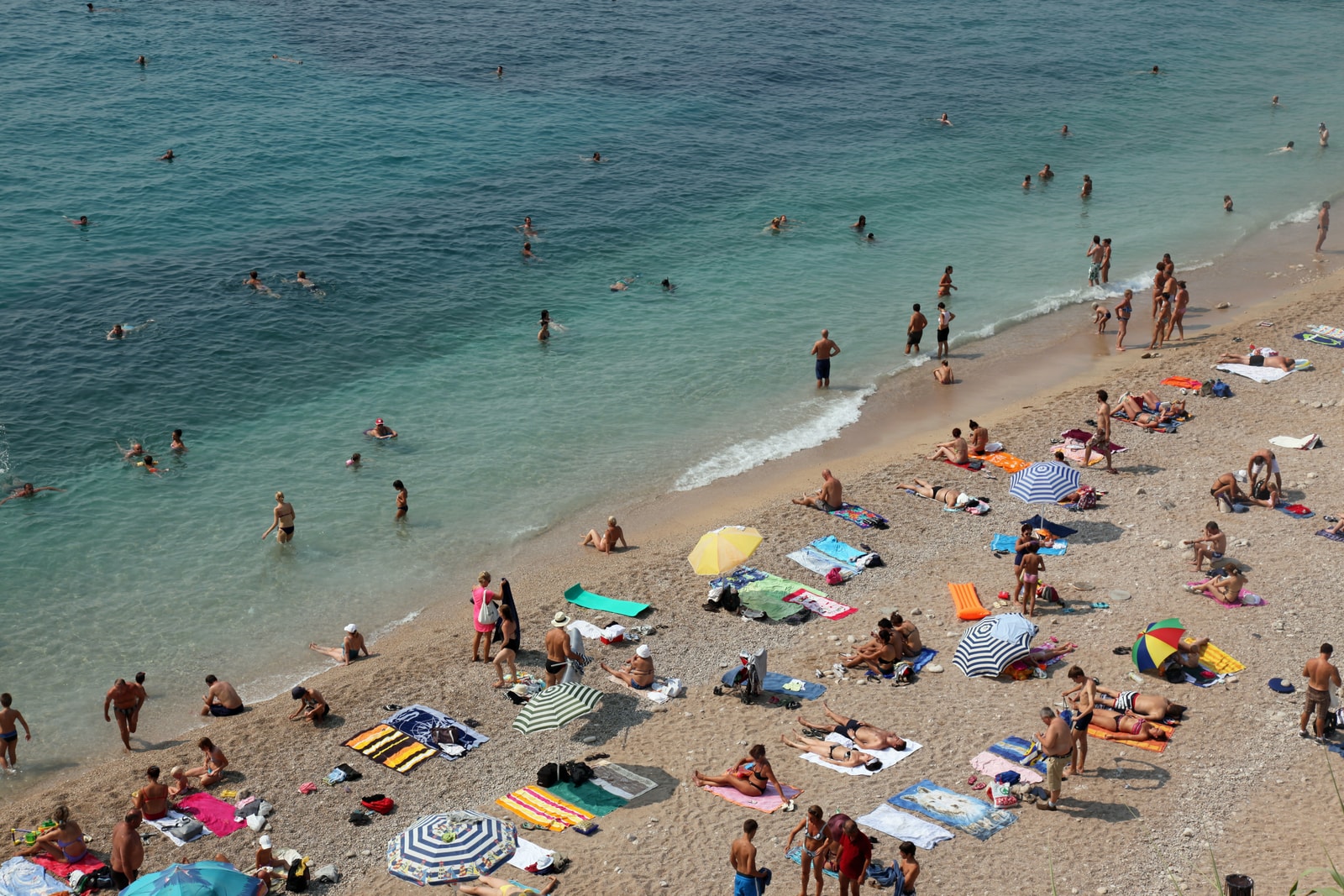 High-angle shot focusing on the energetic beachgoer atmosphere and crystal-clear turquoise waters of Banje Beach.