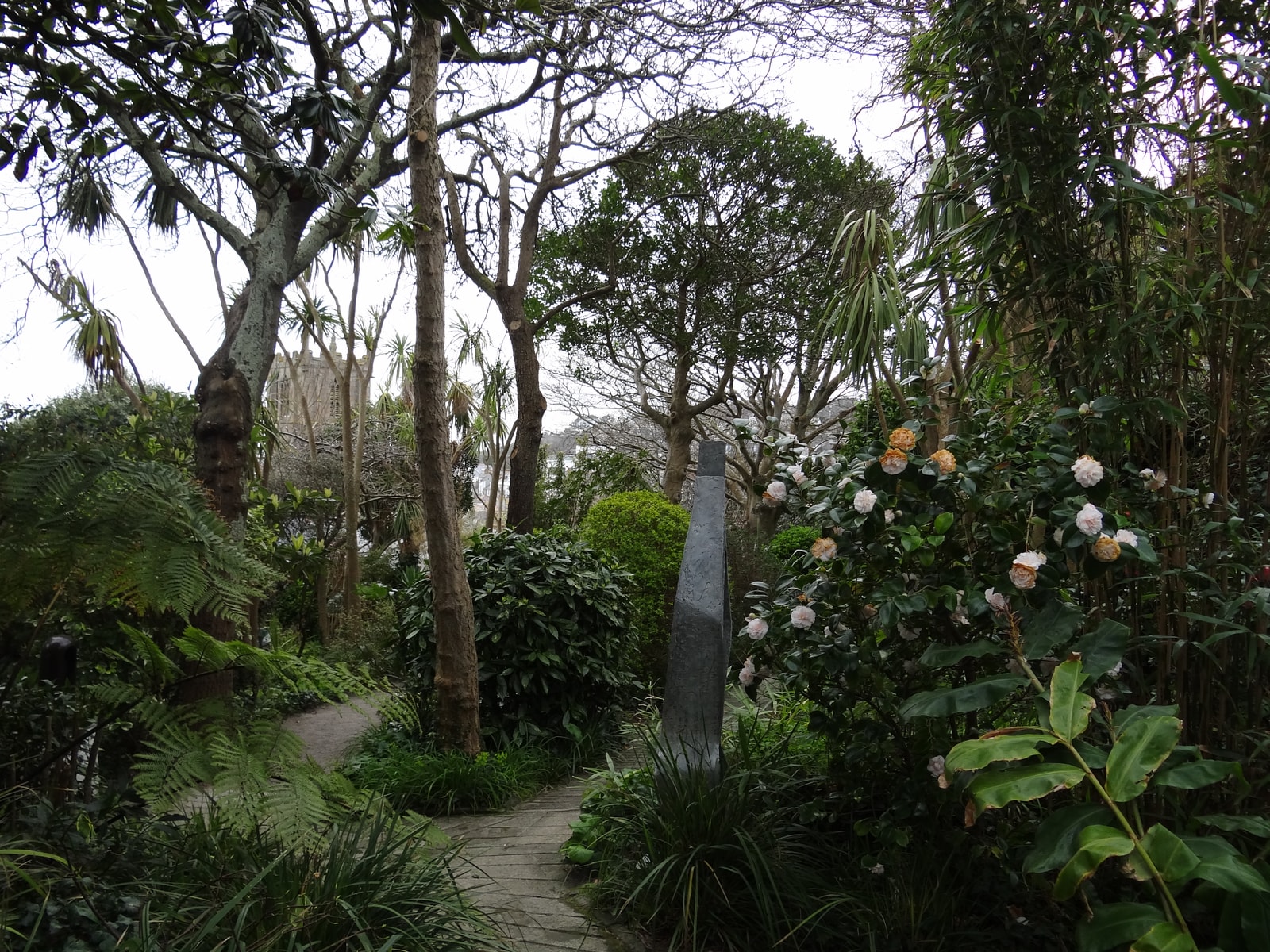 A striking modernist bronze sculpture by Barbara Hepworth stands among lush, tropical-style foliage in her preserved St Ives studio garden.