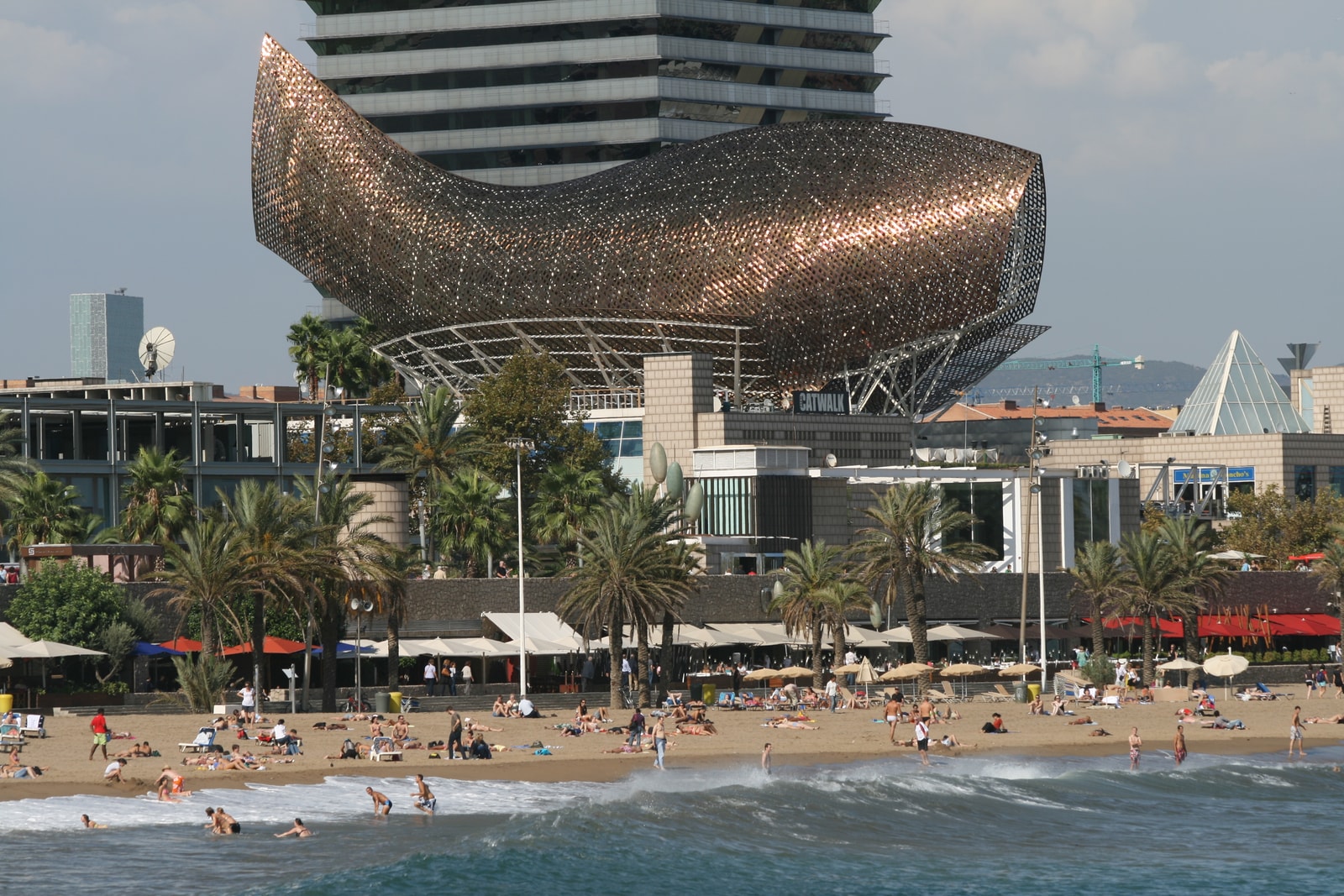 Frank Gehry's giant, golden fish sculpture shimmers in the sun, with modern skyscrapers in the background.