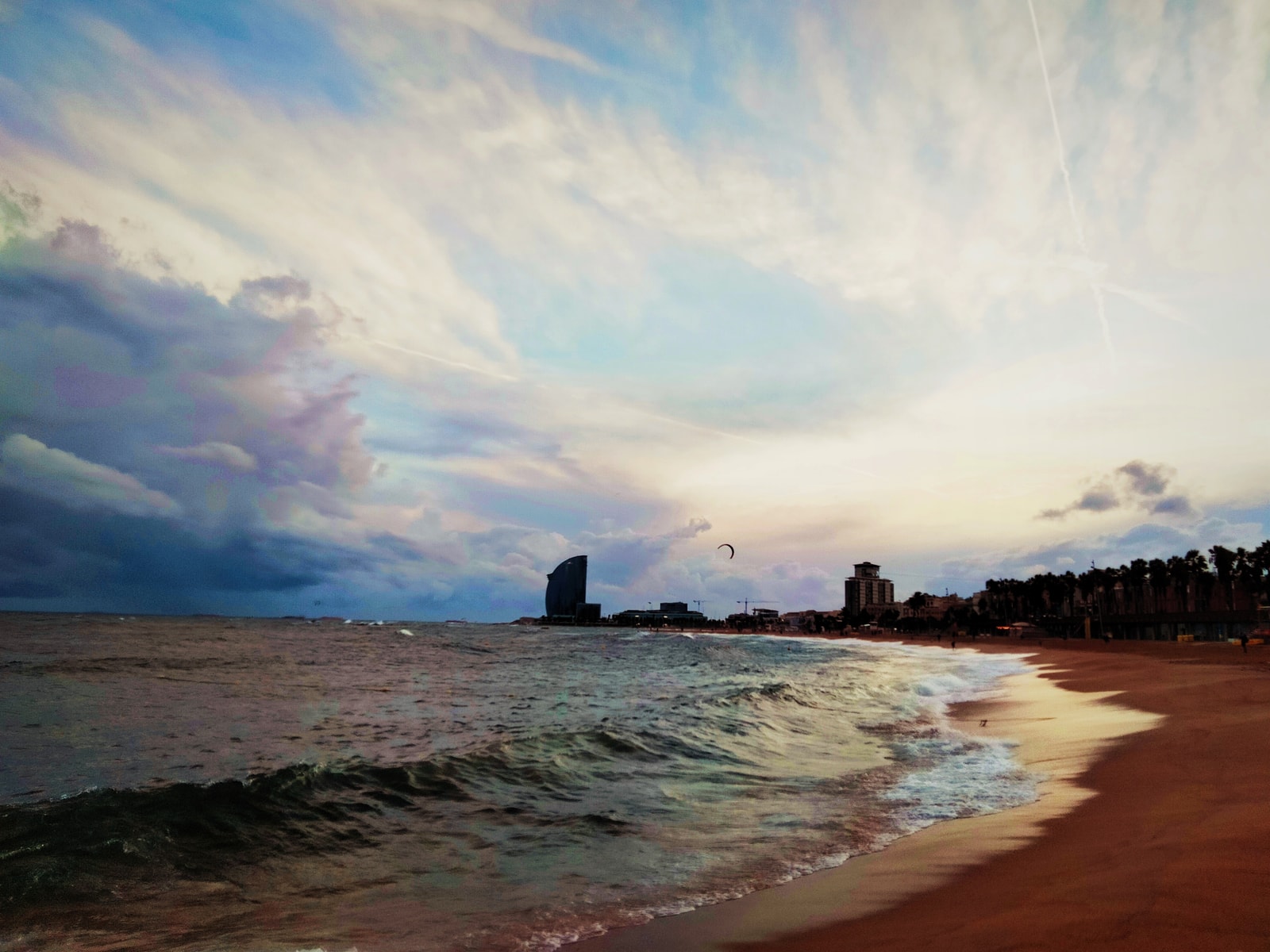 A dramatic sunset view of Barceloneta Beach from the Gas breakwater, with twilight colors filling the sky.