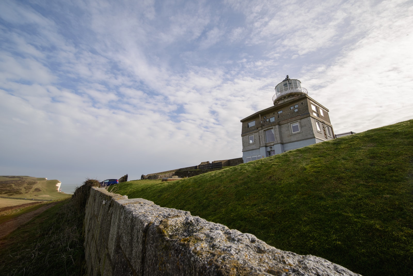The brick Belle Tout Lighthouse stands on the cliff edge, with the red-and-white striped Beachy Head Lighthouse visible in the sea in the background.