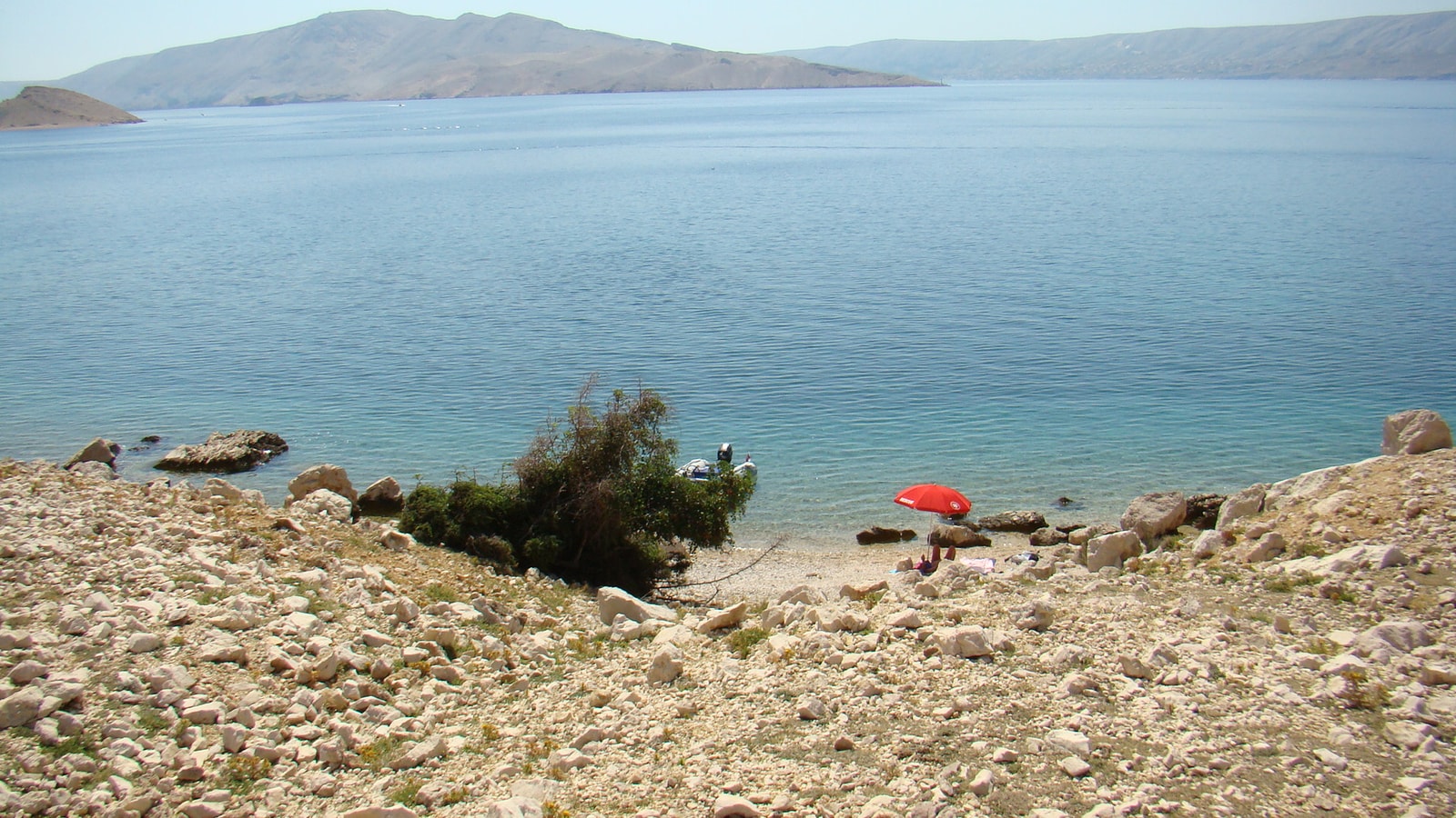 A tiny, isolated cove at Beritnica Beach with a single red umbrella and an anchored boat.