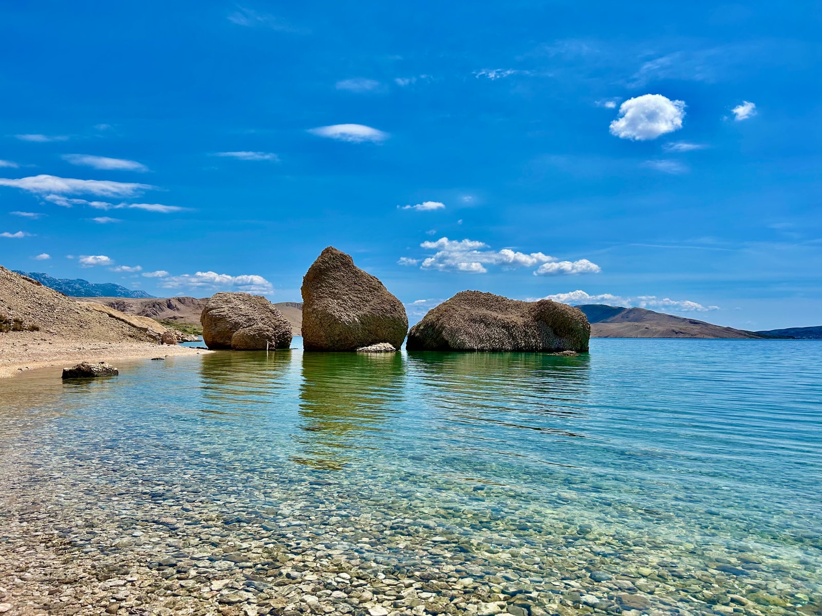 Three massive rock formations rise from the turquoise water at Beritnica Beach, showcasing its unique, rugged terrain.