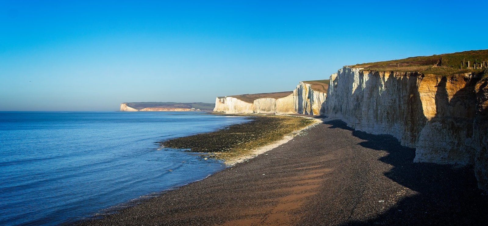 A wide panoramic view of Birling Gap beach with the iconic white Seven Sisters cliffs stretching into the distance.