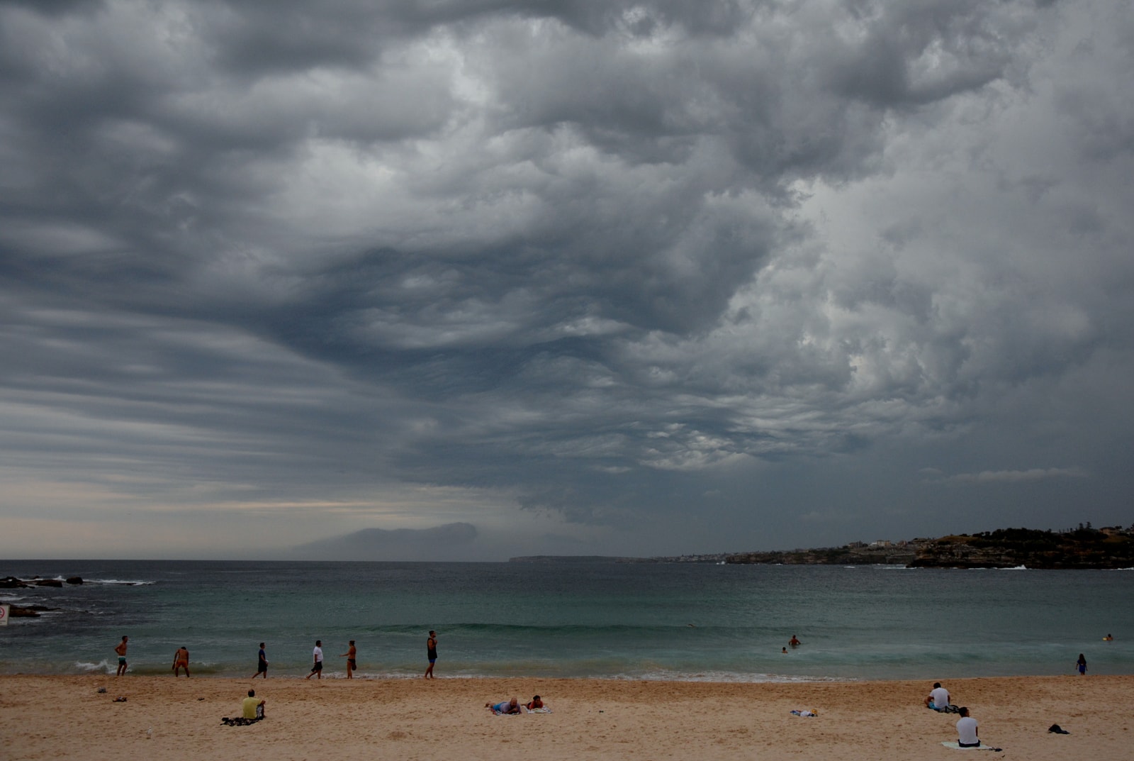 Dark storm clouds gather over Bondi Beach, contrasting with the bright turquoise of the water.
