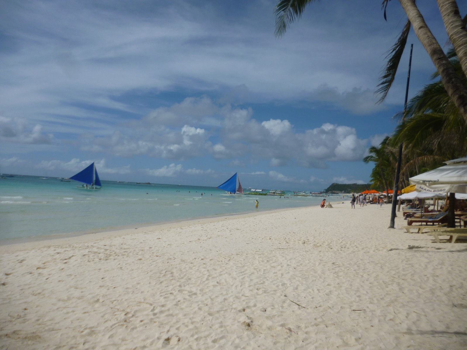A wide view of White Beach with several traditional paraw sailboats moored in the shallow, clear water.