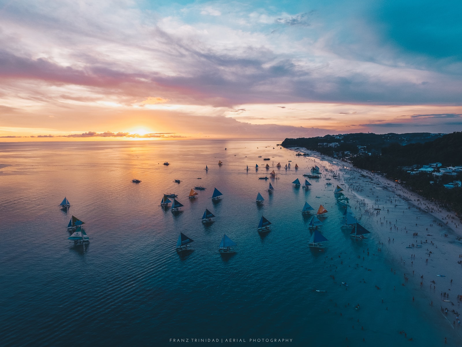 An aerial view of White Beach with numerous boats scattered in the turquoise water near the shore.