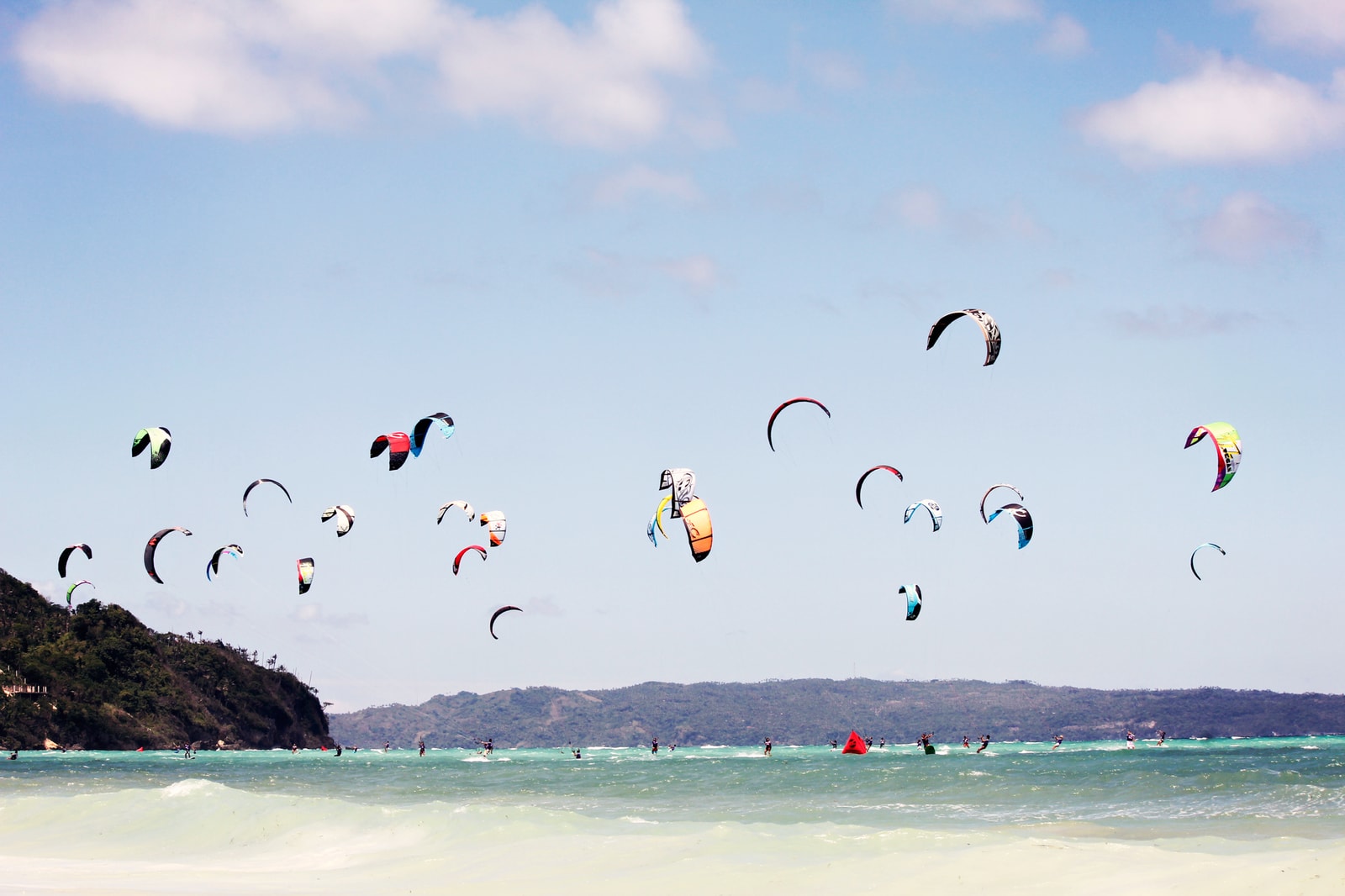 A kitesurfer glides across the water with a colorful kite, illustrating Boracay's reputation for water sports.