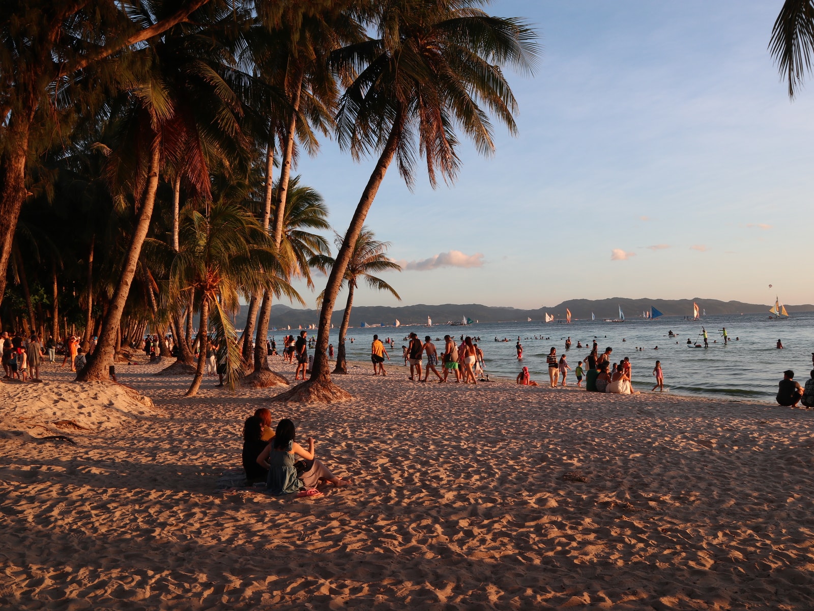 The beach at Station 2 in the evening, with palm trees, boats on the water, and people enjoying the sunset.
