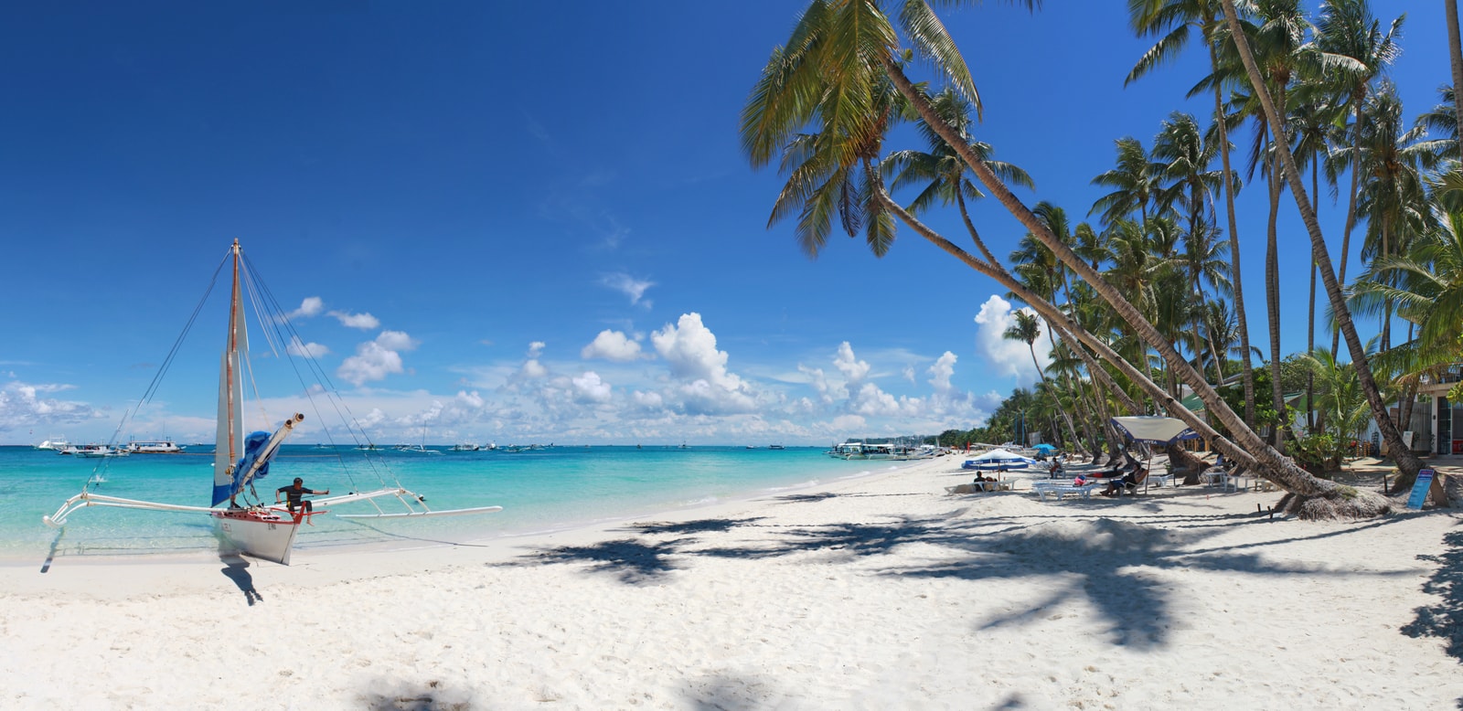 A panoramic view of Station 3 on White Beach, showing a wide expanse of sand, calm blue water, and palm trees.