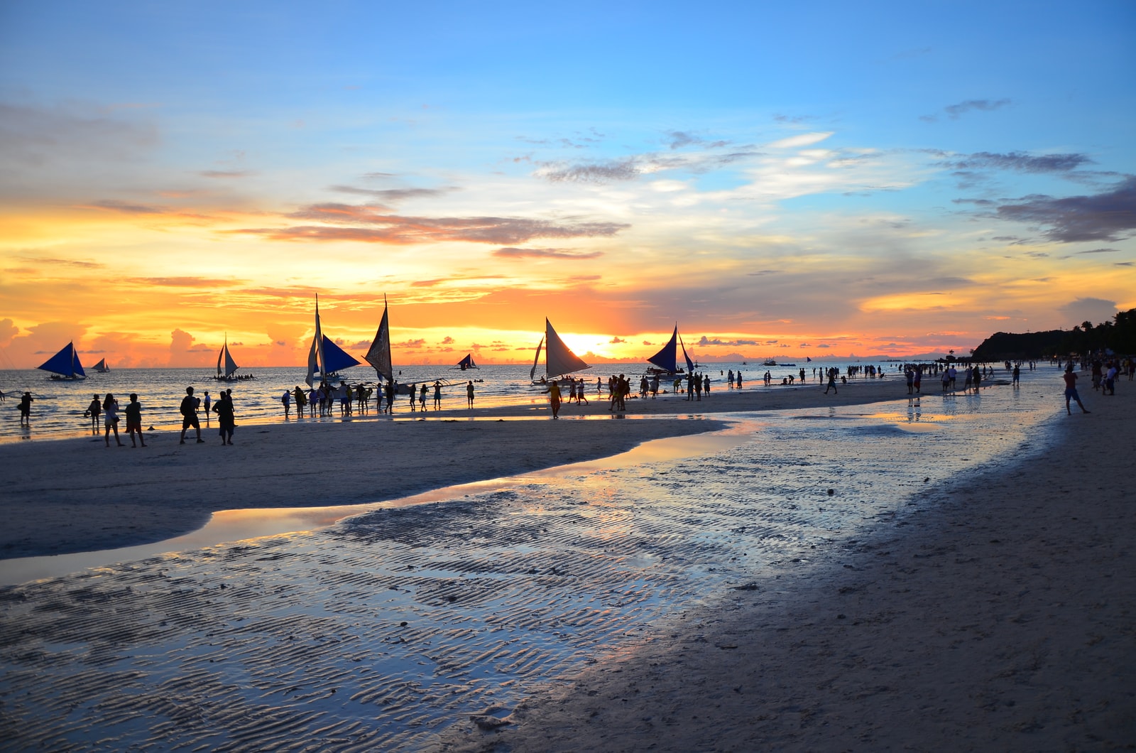 A vibrant sunset scene on White Beach with sailboats on the water and people on the shore.