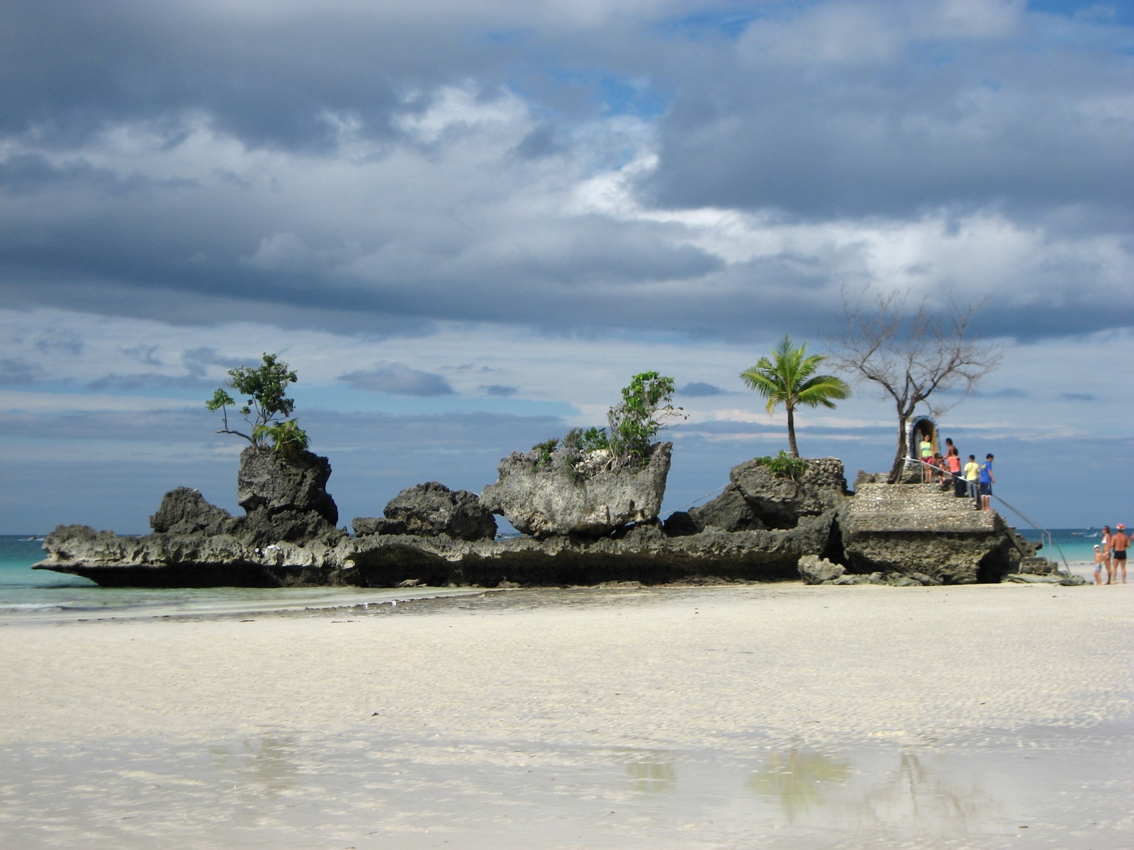 Willy's Rock seen from the beach at low tide, with people walking on the exposed sand around it.