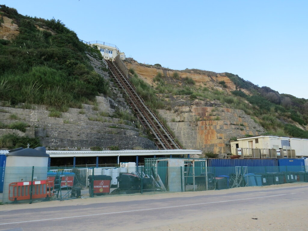A historic funicular car of the East Cliff Railway ascends the steep, green-covered sandstone cliff face in Bournemouth.