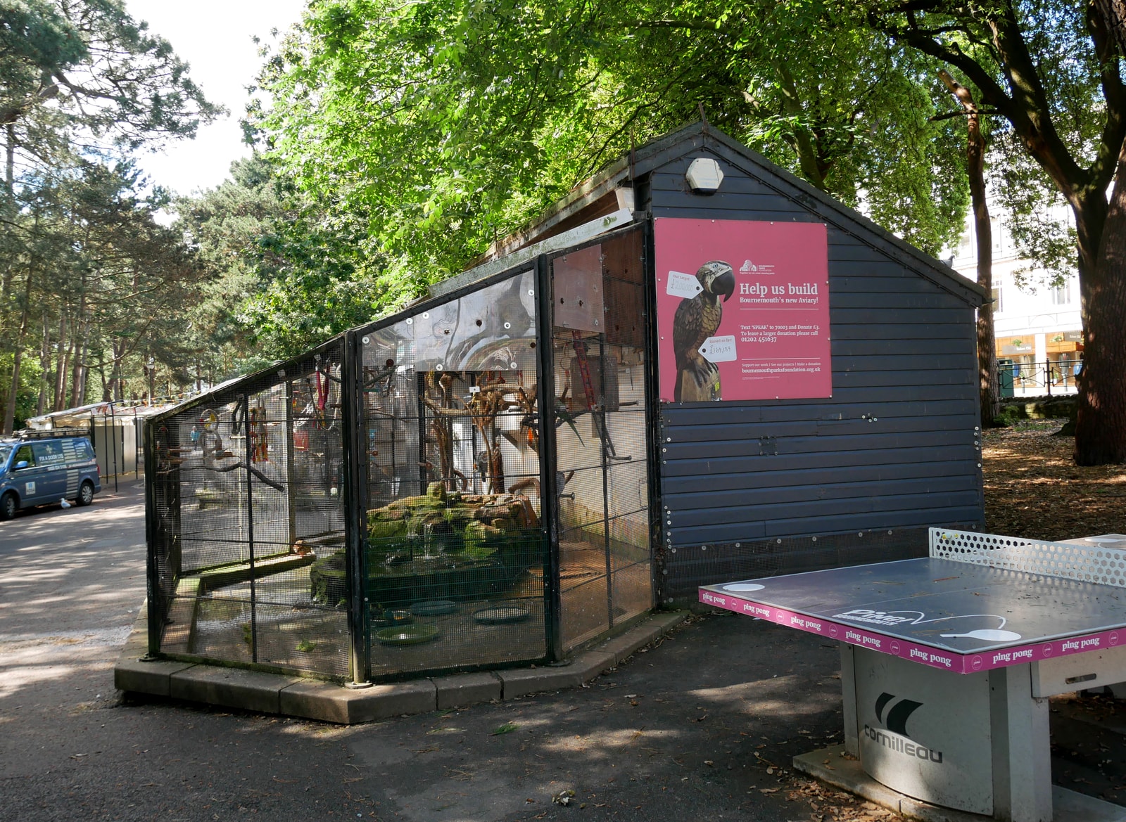 The white structure of the Aviary in Bournemouth's Lower Gardens is surrounded by tall pine trees and lush greenery.