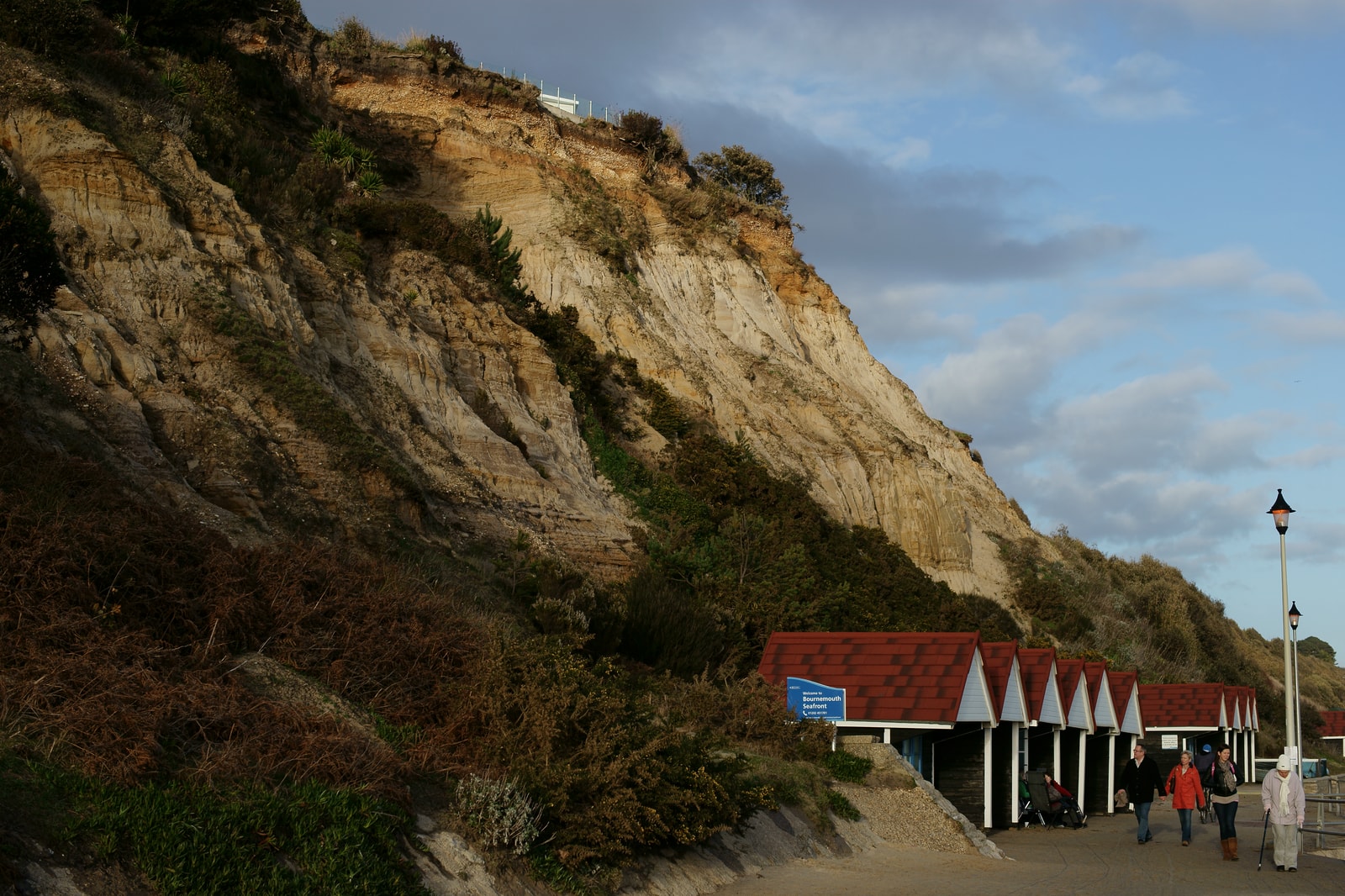 Red-roofed beach huts sit at the base of the dramatic sandstone cliffs and lush greenery of Branksome Chine.