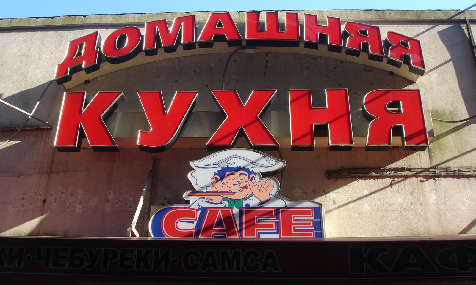 A red sign with Cyrillic lettering for a local cafe, advertising 'Domashnyaya Kukhnya' or 'Homemade Cuisine.'