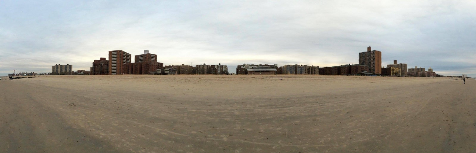A panoramic view from the sand showing Brighton Beach's distinctive skyline of large, mid-rise brick apartment buildings directly fronting the wide beach.
