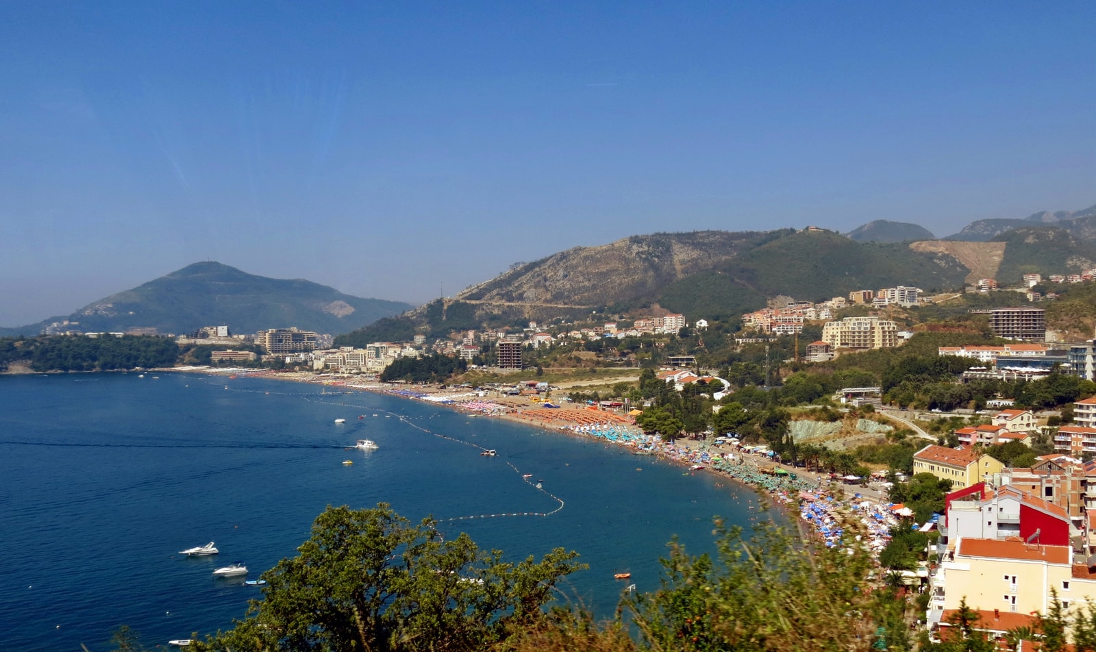A panoramic view of the Budva Riviera coastline, showing its curving bays, resorts, and dramatic mountains.