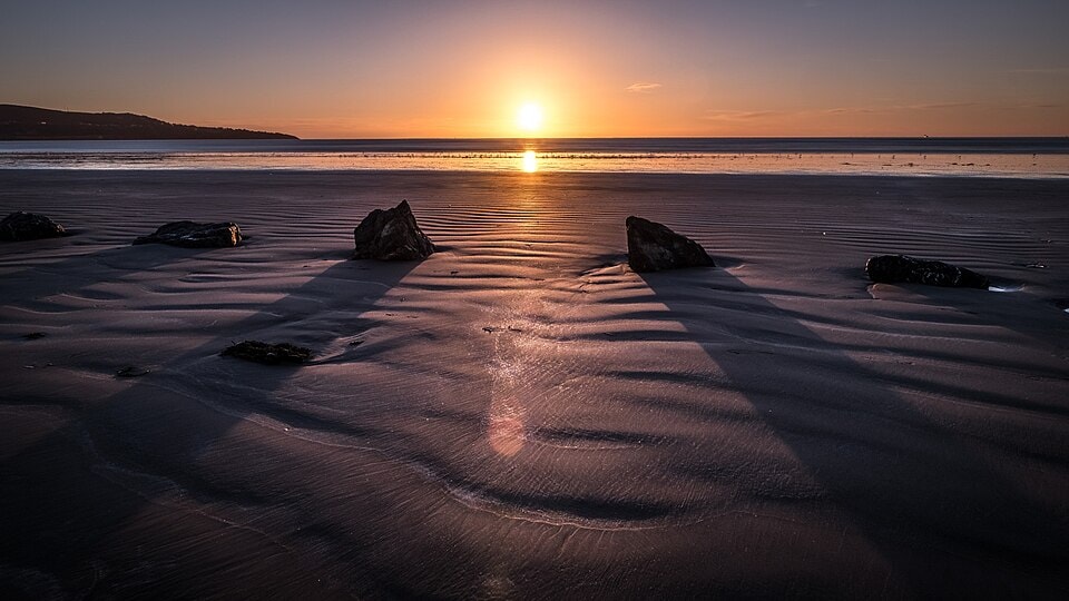 The sun rises over Bull Island, casting a golden light on the wet sand and scattered rocks.