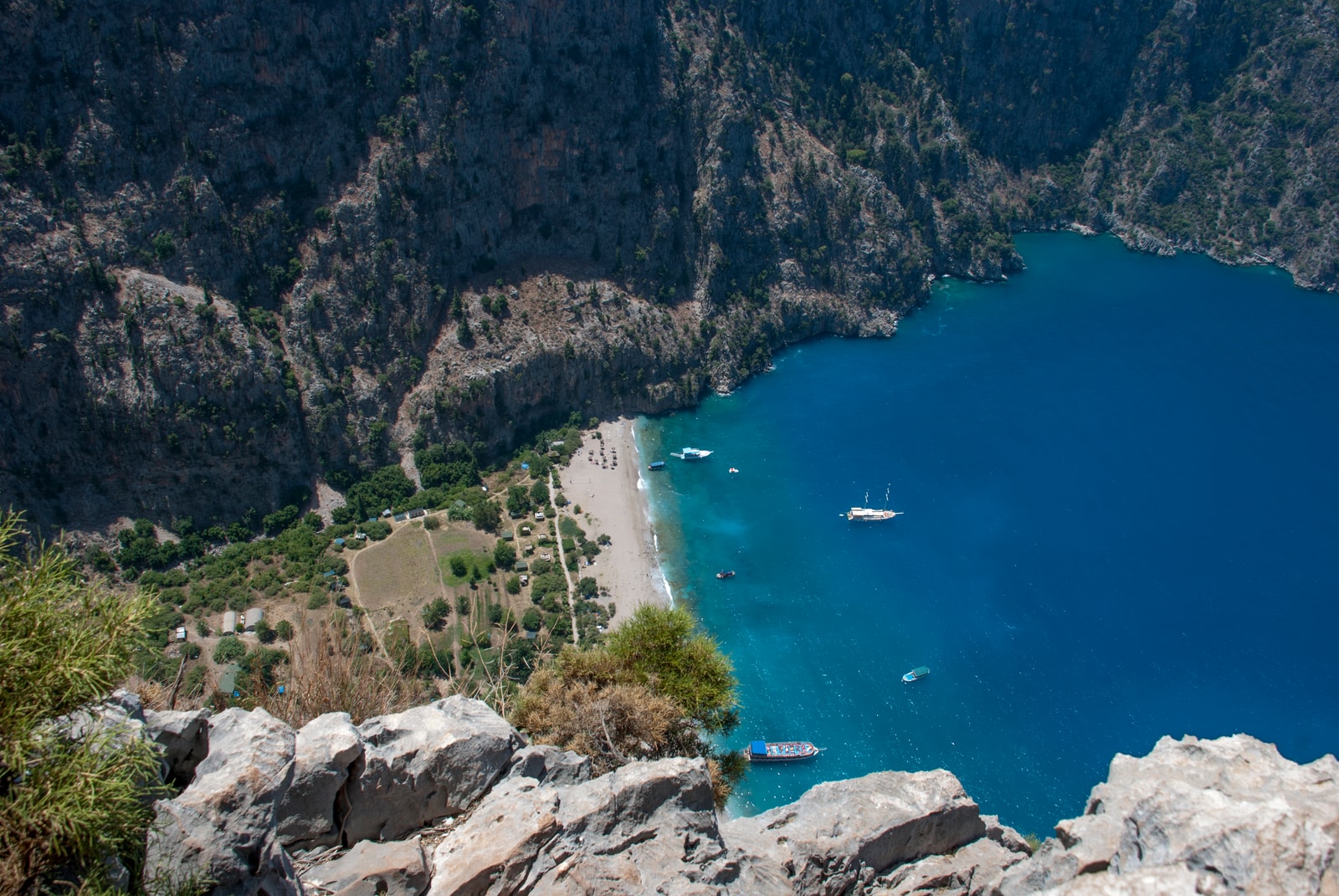 A high-angle view of Butterfly Valley, showing a small beach and turquoise water enclosed by steep, rocky cliffs.