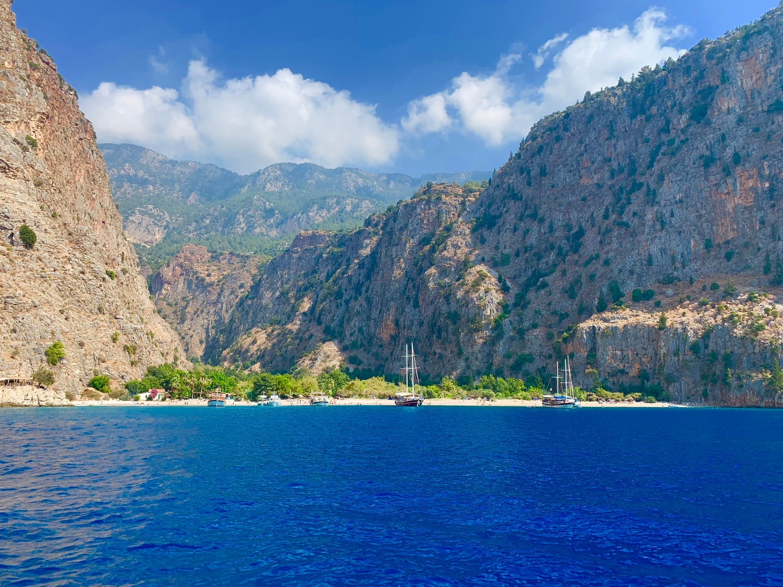 A view from the water looking towards a narrow beach nestled between two towering, steep cliffs.