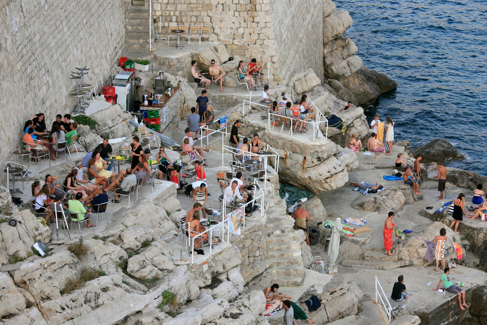 Visitors relax at Buža Bar, where tiered terraces are built directly onto the rugged cliffs below Dubrovnik's massive city walls.