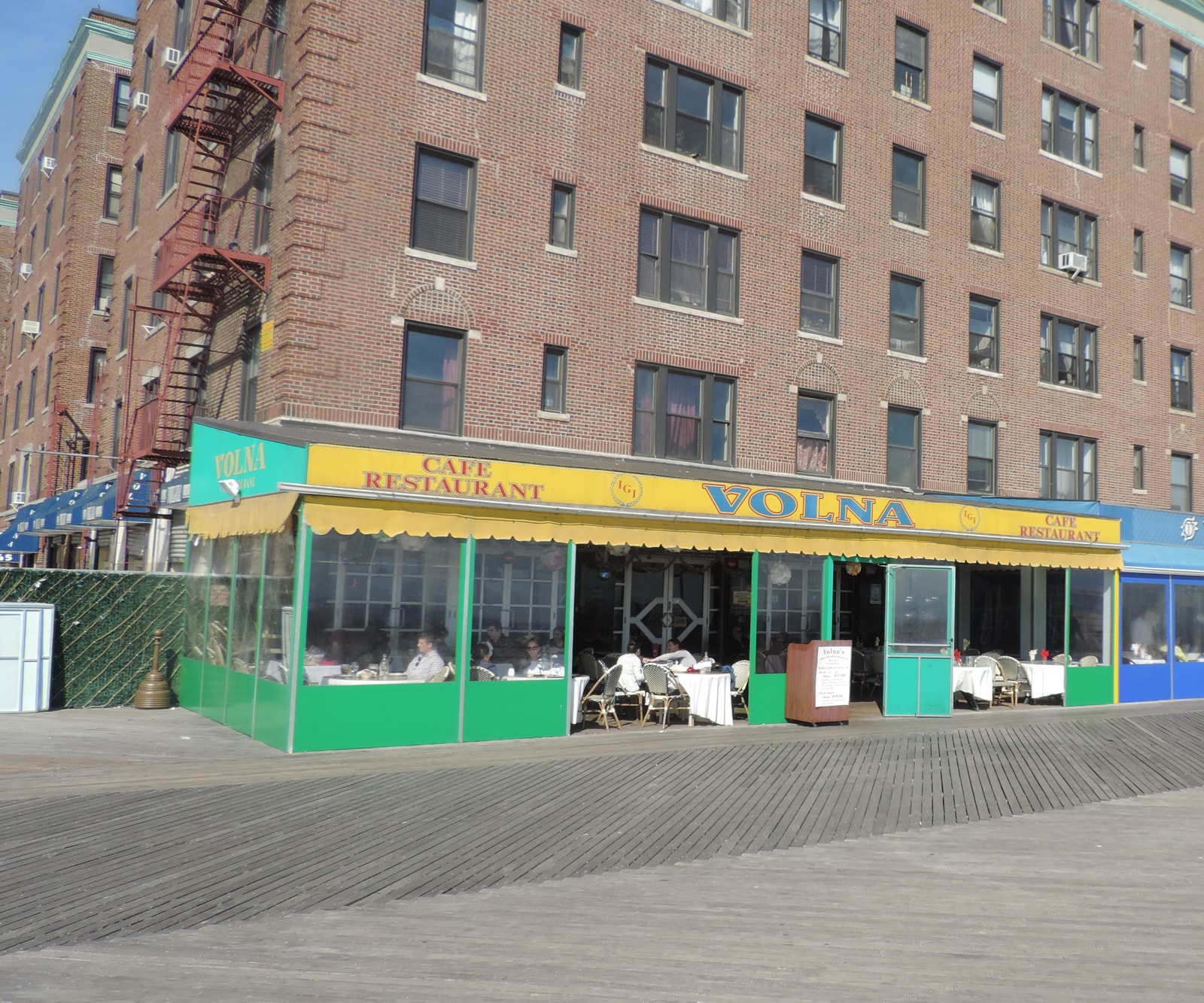 The exterior of Cafe Volna on the Brighton Beach boardwalk, with its bright yellow canopy and an enclosed patio for outdoor dining.