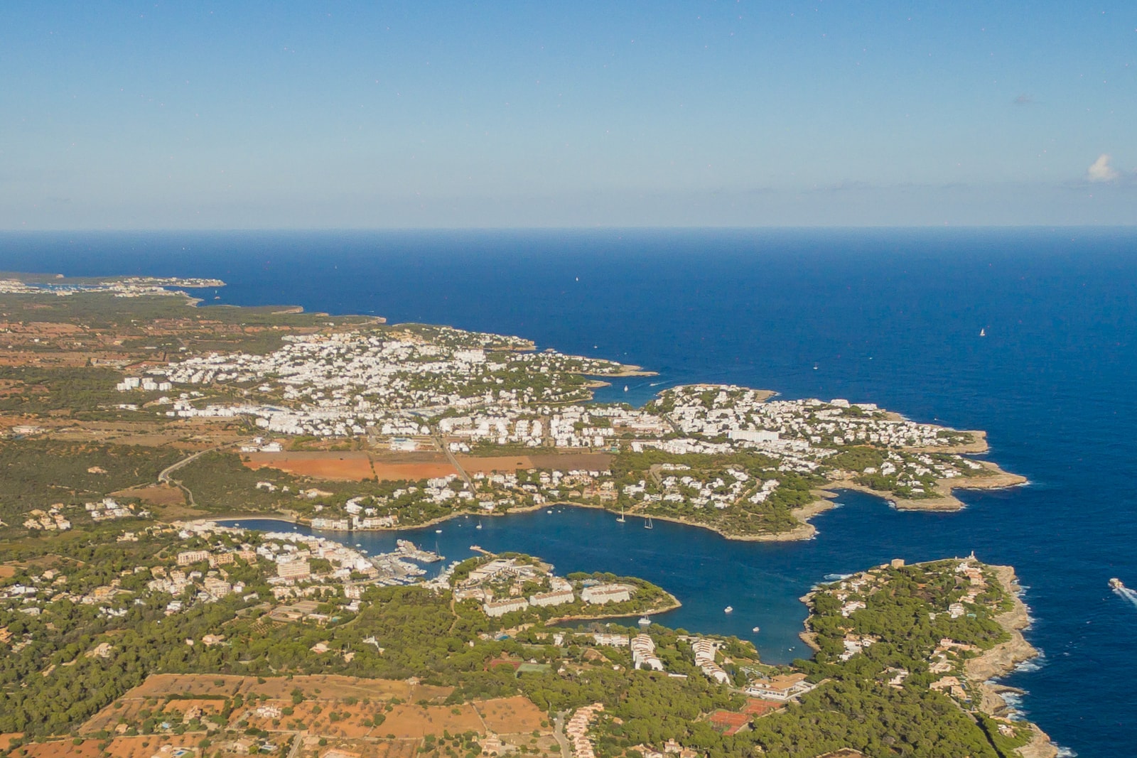 An aerial shot shows the indented coastline of Cala d'Or and Porto Petro, with boats moored in the turquoise waters of the coves and marinas.