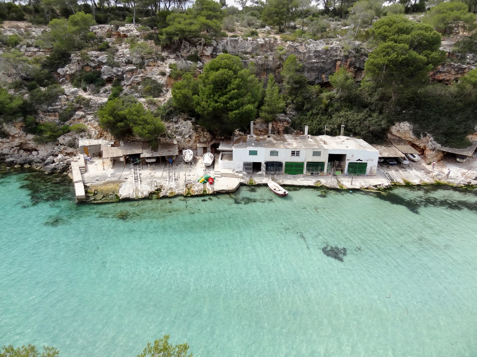Traditional boathouses are built into the rocky edge of a clear-water cove at Cala Pi.