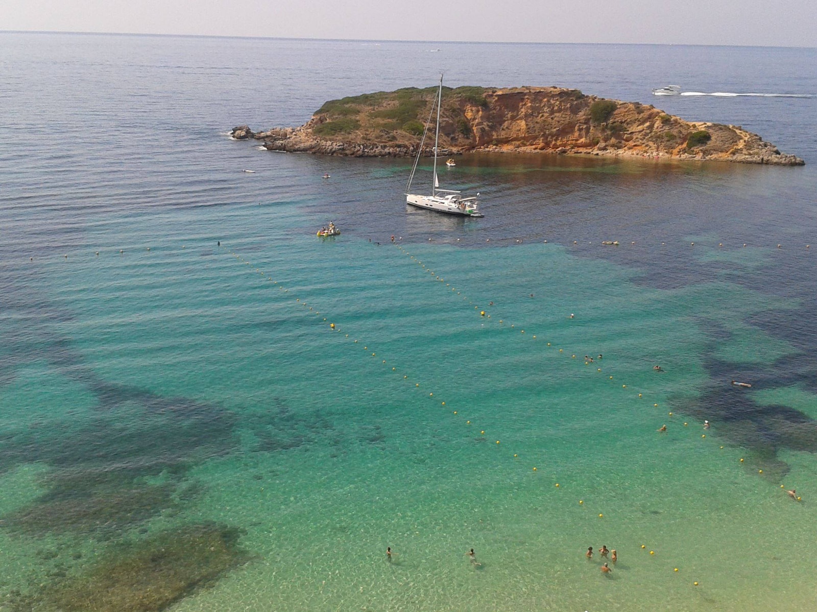 A sailboat floats in the clear water off a rocky headland near Portals Nous.