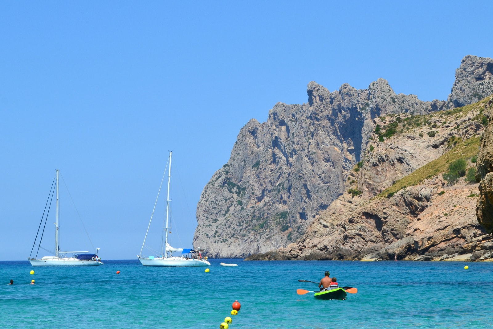 Kayakers paddle in a beautiful cove with clear turquoise water, surrounded by dramatic limestone cliffs.