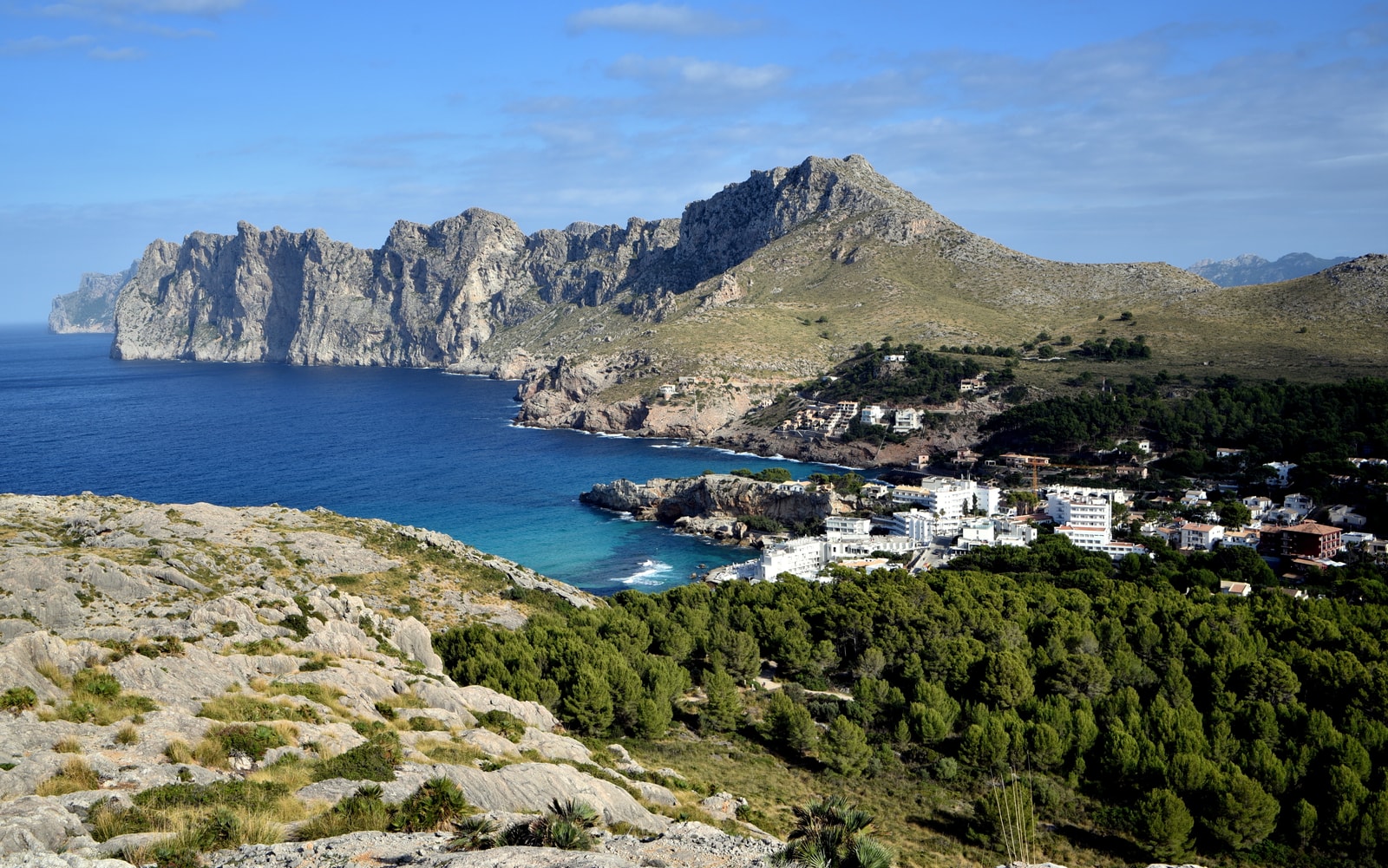 A panoramic view shows a small coastal town nestled between rugged mountains and a series of coves with turquoise water.