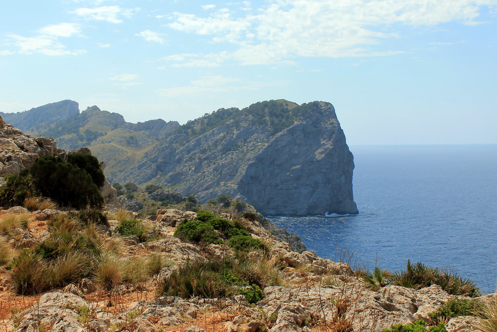 A view from a high vantage point of a rugged, rocky coastline with layered headlands meeting the deep blue sea.